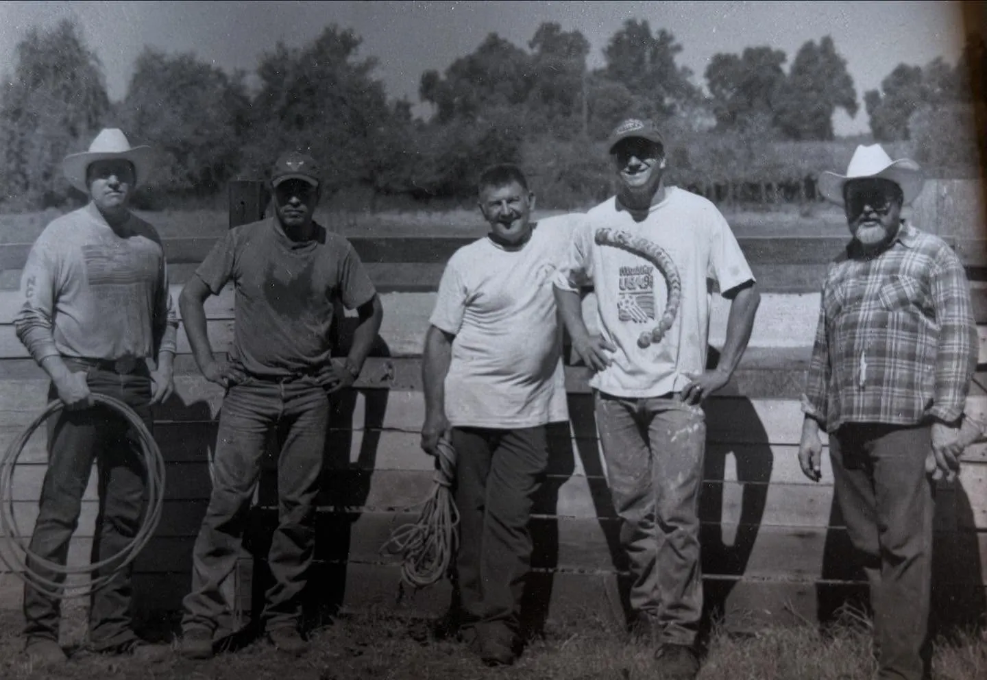 Black and white photo of five men from the Vaccaro family standing at a ranch fence with ropes after branding cattle